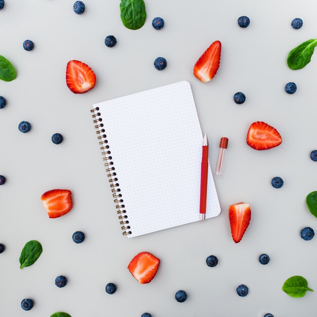 Caderno vazio com morangos e mirtilos em fundo cinza