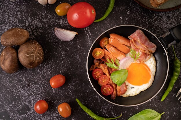 Café da manhã com ovos fritos, salsicha e presunto em uma panela com tomate. Pimenta e manjericão