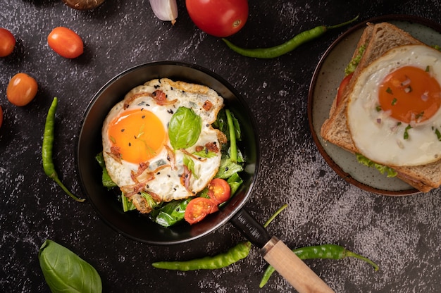 Café da manhã com ovos fritos, salsicha e presunto em uma panela com tomate. pimenta e manjericão