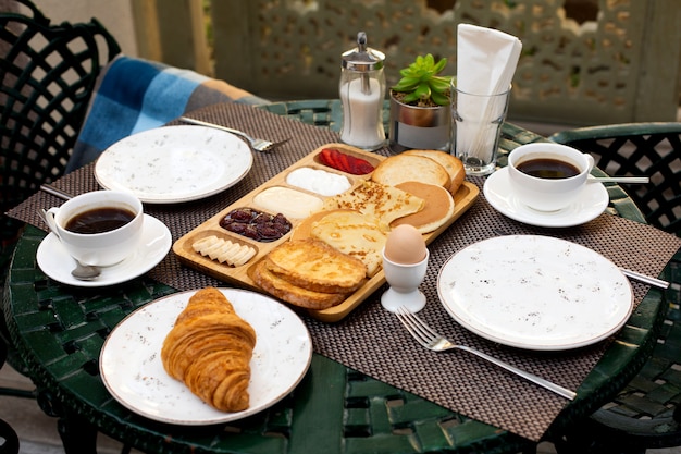 Café da manhã com panquecas de crepes, torradas, croissant, ovo, morangos fatiados, banana e café