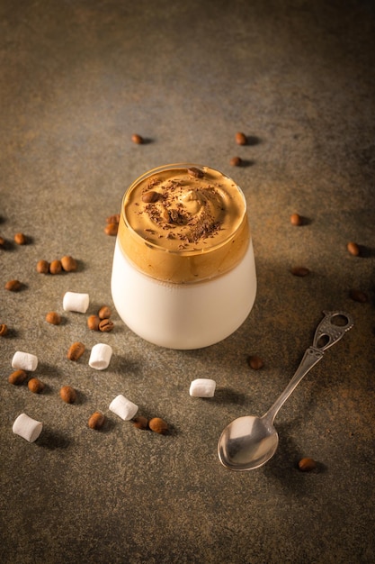 Café dalgona caseiro em fundo escuro ao lado de grãos de café e marshmallows fofos na moda Foto Premium