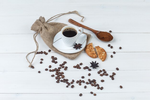 Café de vista de alto ângulo na xícara com café moído, especiarias, grãos de café, biscoitos em madeira e fundo de saco. horizontal