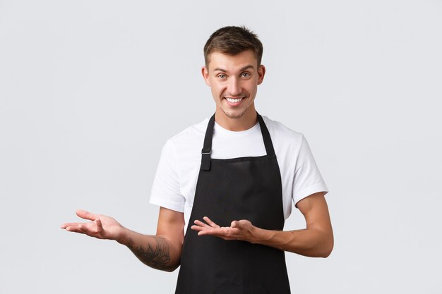 Café e restaurantes, donos de cafeterias, conceito de varejo. Vendedor bonitão e atrevido, garçom de avental preto apontando para a esquerda, convidando a entrar, mostrando ou introduzindo descontos, fundo branco