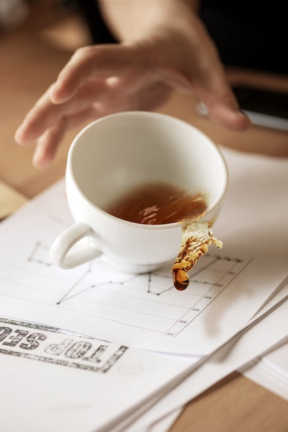 Café em copo branco, derramando sobre a mesa no dia útil da manhã na mesa de escritório