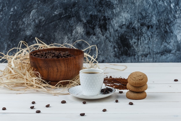 Café em uma xícara com café moído, grãos de café, especiarias, vista lateral de biscoitos em fundo de madeira e grunge