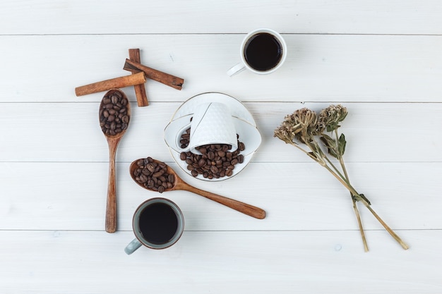 Café em xícaras com grãos de café, paus de canela e ervas secas, vista superior em um fundo de madeira