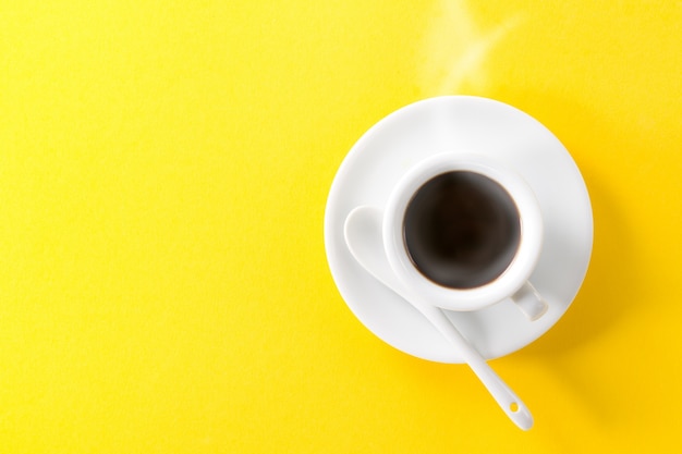 Café expresso em copo de vapor quente de cerâmica branca pequena em fundo amarelo vibrante. mínimo alimento conceito de energia da manhã.