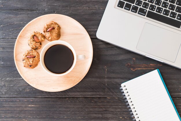 Café preto e biscoitos com laptop e livro de notas