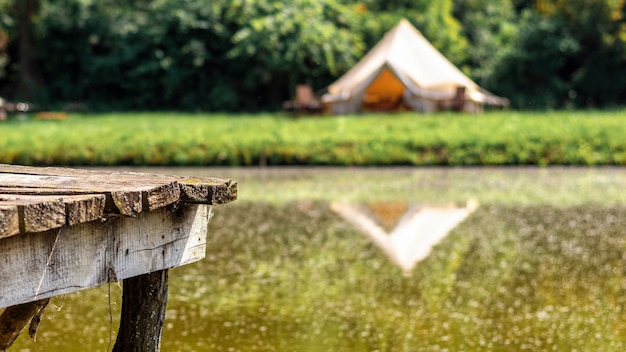 Cais de madeira para descansar perto de um lago com tenda no fundo em glamping. Natureza, vegetação ao redor