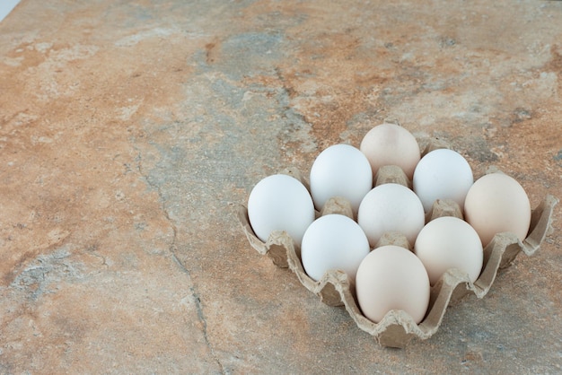 Caixa de papelão com ovos brancos frescos de frango na mesa de mármore.