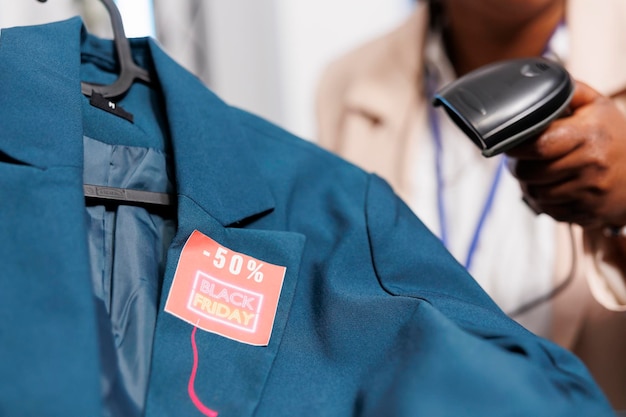 Foto grátis caixa feminina segurando um scanner de código de barras escaneando a etiqueta de preço da sexta-feira negra em roupas, servindo clientes no balcão de checkout. conceito de vendas sazonais, descontos de feriado na loja de roupas