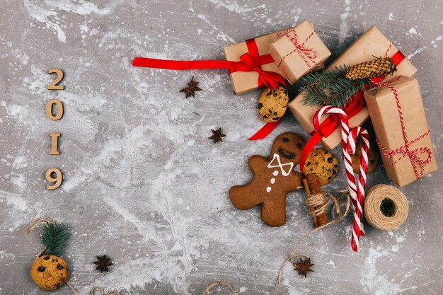 Caixas de presente marrom cinza com fitas vermelhas estão no chão com bolachas de chocolate, pães de gengibre e corda antes do número 2019