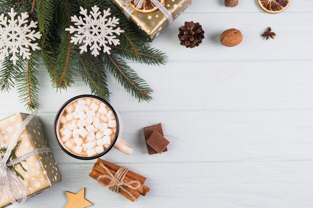 Caixas de presentes no envoltório de Natal perto de copo com marshmallows e ramo de abeto