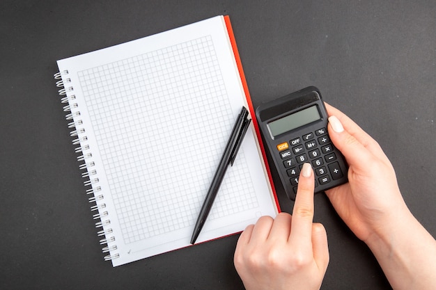 Calculadora de bloco de notas espiral com vista superior em caneta de mão feminina no escuro