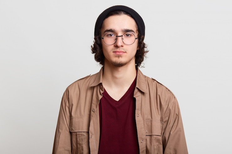 Foto grátis calma garoto de cabelo encaracolado bonito posando isolado em cinza claro, parado, parece pacífico, vestindo de maneira casual. conceito de juventude e estilo.