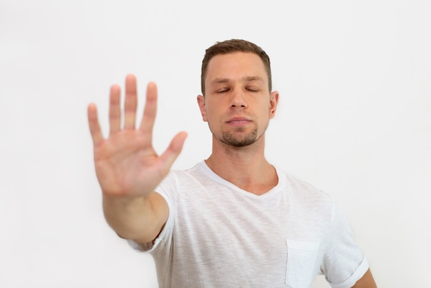 Calma jovem bonito com os olhos fechados, fazendo o gesto de parada