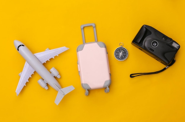 Cama plana de viagem. mini mala de viagem de plástico, câmera, avião e bússola em fundo amarelo. estilo mínimo. vista do topo