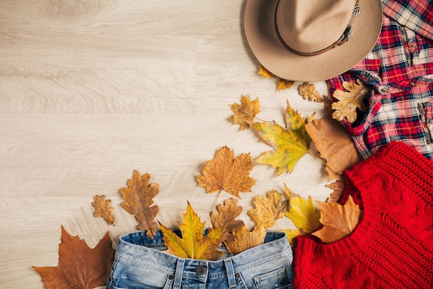 Camada plana de estilo feminino e acessórios, suéter de malha vermelha, camisa quadriculada, jeans, chapéu, tendência da moda outono, vista de cima, roupas, folhas amarelas