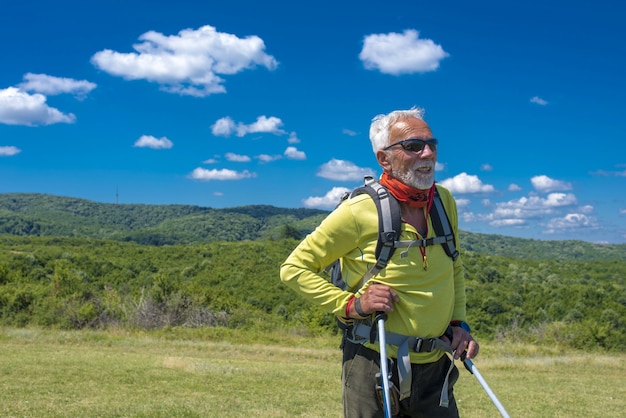 Caminhante masculino em pé e sorrindo em um prado na montanha