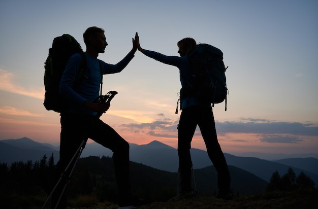 Caminhantes de casal jovem dando mais cinco durante o pôr do sol nas montanhas