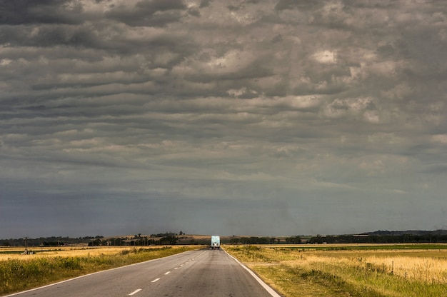 Caminhão na estrada cercada por campos vazios sob o céu nublado