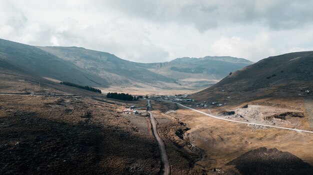 Caminho no meio das montanhas perto de uma casa sob um céu nublado