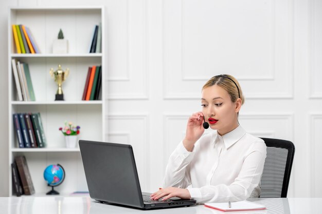 Camisa de escritório loira bonita de atendimento ao cliente com fone de ouvido e computador falando com um cliente