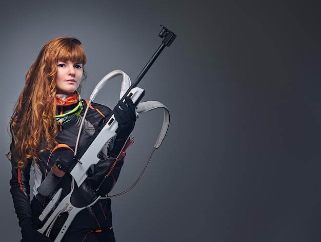 Foto grátis campeã de biatlo feminino ruiva mirando com uma arma competitiva em um estúdio sobre fundo cinza. campeã de biatlo feminino ruiva mirando com uma arma competitiva em um estúdio sobre fundo cinza.