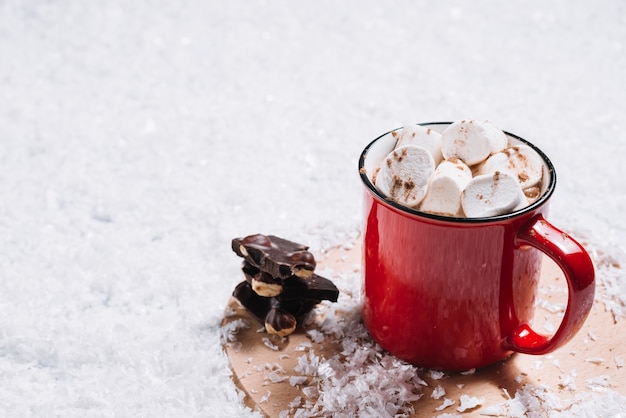 Caneca com marshmallows perto de chocolate em stand entre a neve