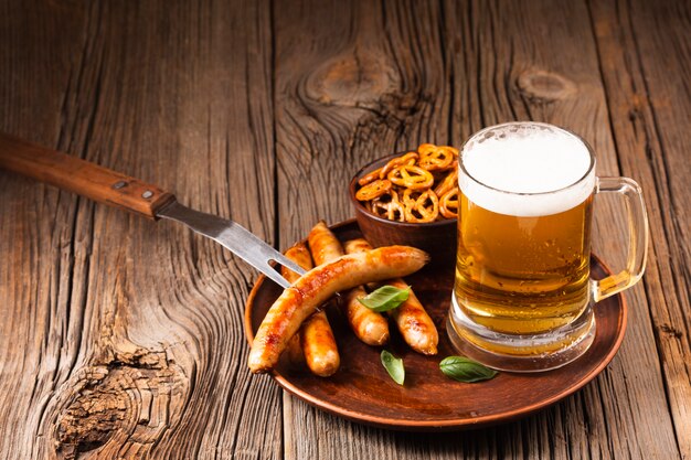 Caneca de cerveja com linguiça e lanches na placa de madeira