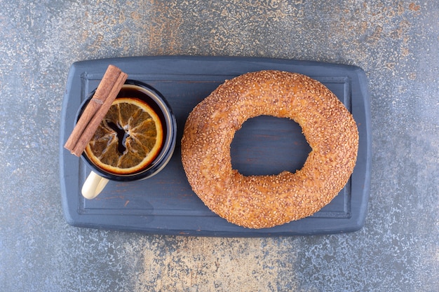 Foto grátis caneca de chá de metal com rodela de limão seco, pau de canela e bagel em uma placa sobre superfície de mármore