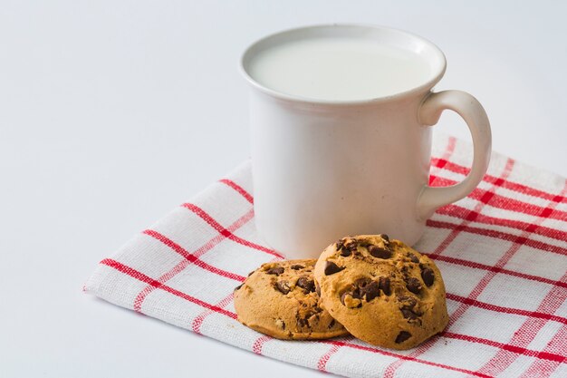Caneca de leite com biscoitos no guardanapo sobre o fundo branco