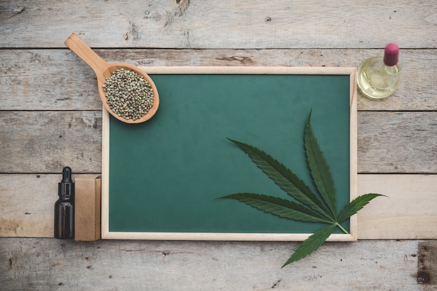 Cannabis, sementes de maconha, folhas de maconha, colocadas na placa verde E há óleo de cânhamo ao lado no chão de madeira.
