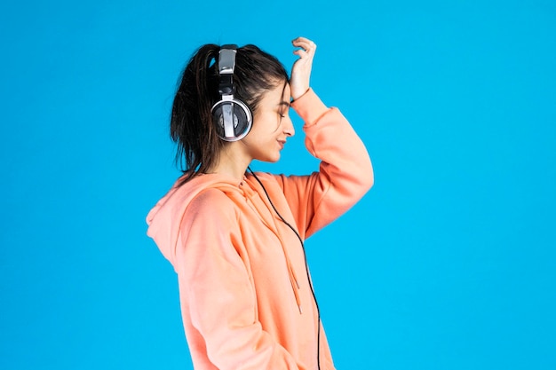 Cansado de mulheres usando fones de ouvido e ouvindo música em fundo azul