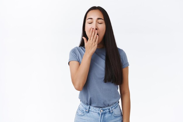 Cansado e bonito estudante asiático odeia acordar cedo bocejando e cobrir a boca com a palma fechar os olhos esperando o café no café em pé com sono sobre fundo branco expressar tédio