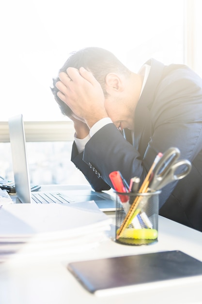 Cansado jovem empresário com laptop no seu local de trabalho