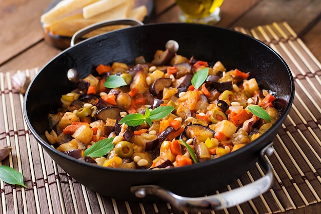 Caponata italiana com frigideira em uma mesa de madeira