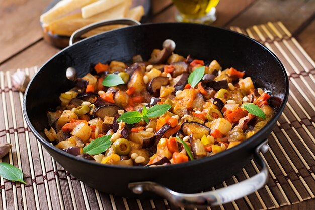 Caponata italiana com frigideira em uma mesa de madeira