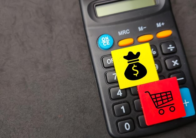 Captura aproximada de dois quadrados de madeira coloridos com ícones de compras e dinheiro numa calculadora preta