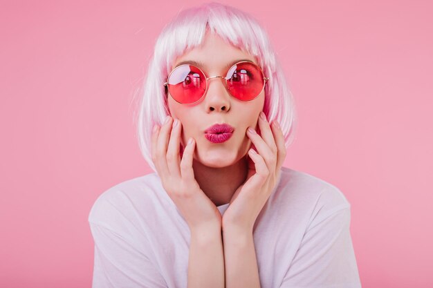 Captura aproximada de uma linda mulher bem-humorada em óculos de sol cor-de-rosa Foto interior de uma jovem europeia que usa peruke