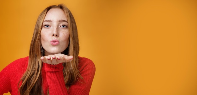 Captura aproximada de uma ruiva sensual e atraente em roupas de malha vermelha dobrando os lábios inclinando-se para