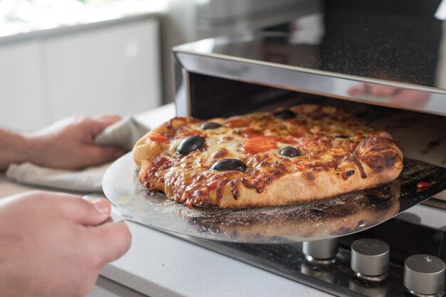 Captura de uma mão de cozinheiro masculino removendo pizza assada do forno