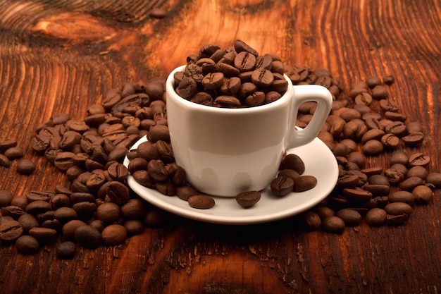 Captura de uma xícara branca cheia de grãos de café em uma mesa de madeira