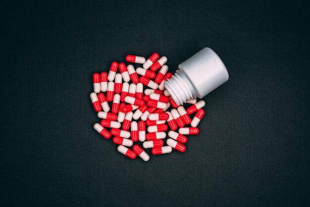 Captura de vista superior de cápsulas vermelhas e brancas caindo do pequeno frasco de comprimidos no fundo escuro