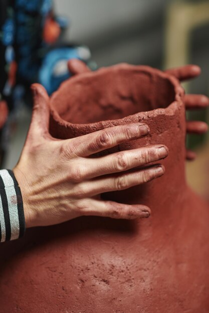 Captura vertical de mãos esculpindo um vaso de barro com rosto