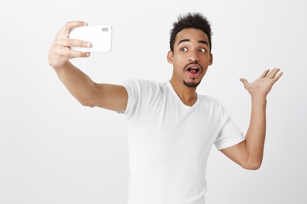 Cara afro-americano bonito mostrando algo enquanto tira uma selfie