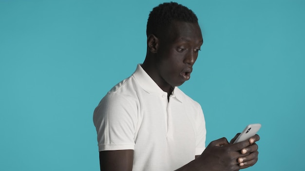 Foto grátis cara afro-americano chocado parecendo espantado comprando mercadorias à venda usando smartphone para compras on-line sobre fundo colorido conceito de tecnologia