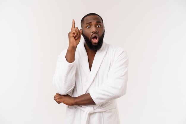 Cara afro-americano vestindo um roupão apontando o dedo com surpresa e emoção feliz isolado sobre fundo branco