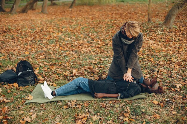 Cara ajuda uma mulher. Garota africana está deitada inconsciente. Prestando primeiros socorros no parque.