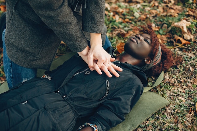 Foto grátis cara ajuda uma mulher. garota africana está deitada inconsciente. prestando primeiros socorros no parque.